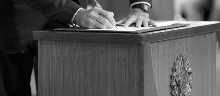 Homem assinando um contrato em uma mesa de discursos.