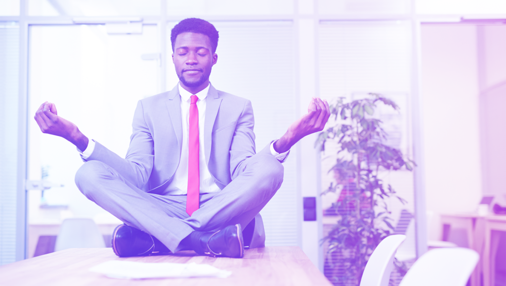 Homem meditando em cima de uma mesa em um escritório